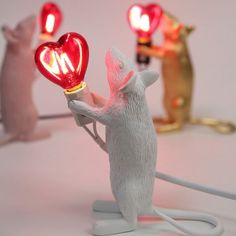 a white mouse holding a red light up in the shape of a heart with two mice standing next to it