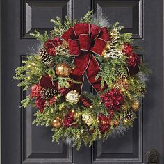 a christmas wreath with red and gold decorations on the front door, decorated with pine cones