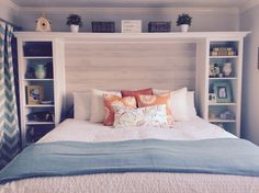 a white bed with blue and orange pillows in a room next to bookshelves