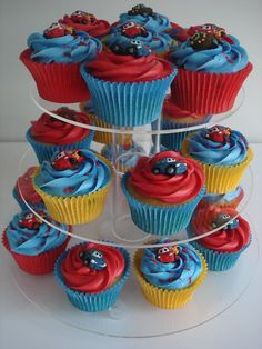 cupcakes with blue frosting and red icing are stacked on a clear cake plate