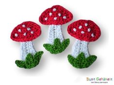 three crocheted mushrooms sitting on top of each other in green leaves and white dots