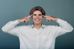 a man in a white shirt is holding his hands up to his ears and smiling