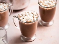 three mugs filled with hot chocolate and marshmallows on top of a table