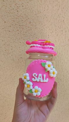 a hand holding a jar with flowers and the word sale written on it in pink frosting