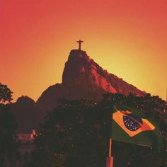 a cross on top of a mountain with a flag flying in the foreground at sunset