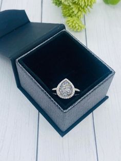 an open box with a ring in it on a white wooden table next to flowers