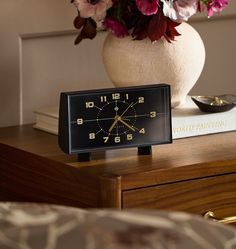 a clock sitting on top of a table next to a vase with flowers in it