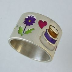 a silver ring with flowers and hearts painted on the side, sitting on a white surface