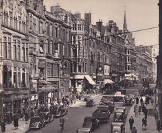 an old black and white photo of cars driving down a city street with tall buildings