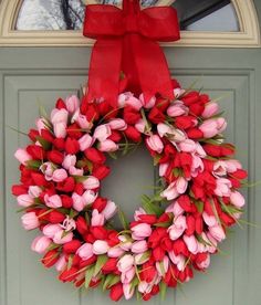 a wreath with red and pink tulips is hanging on a green front door