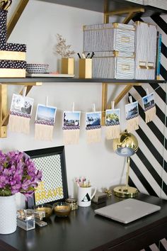 a desk with pictures hanging on the wall and flowers in a vase next to it