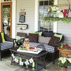 the front porch is decorated with black and white checkered couches, green pillows, and potted plants