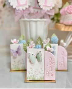 three small cards with butterflies on them sitting in front of a vase filled with flowers