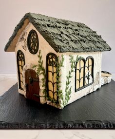 a small house made out of clay on top of a black board with ivy growing around it