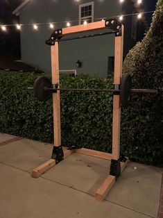 a barbell squat station with lights on the side and bushes in the back ground