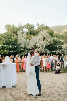 a bride and groom dance together in front of an outdoor wedding party with white linens