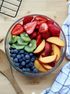 a glass bowl filled with sliced fruit on top of a wooden table next to a spoon