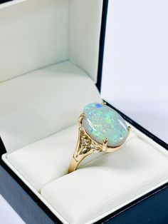 This remarkable gold ring features a large opal with vibrant flashes of green, blue, and yellow, creating a mesmerizing display of color. The bold opal is securely set in a beautifully crafted 9ct gold band, adorned with delicate detailing and brilliant cut diamond set on each sidemaking this ring a standout piece. Opal weight 5.85ct Diamond weight .03ct Ring size Q Approximately weighs 4.8gm Luxury Artisan Opal Ring For Gift, Luxury Gold Opal Ring With Diamond Accents, Diamond Set, Opal Ring, Blue And Yellow, Gold Band, Opal Rings, Brilliant Cut Diamond, Gold Bands