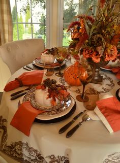 the table is set with dishes, silverware and pumpkins