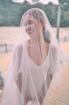 a woman wearing a wedding veil and smiling at the camera while standing on a sidewalk