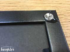 an empty black frame with a silver flower on it sitting on a wooden table top