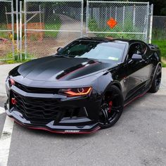 a black chevrolet camaro parked in front of a fence