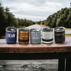 four cans of beer sitting on top of a wooden table next to a road and trees