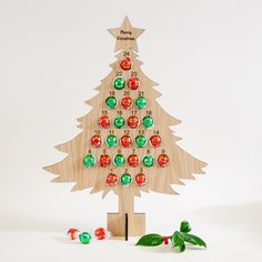 a wooden christmas tree with colorful balls on it's side and green leaves around the base