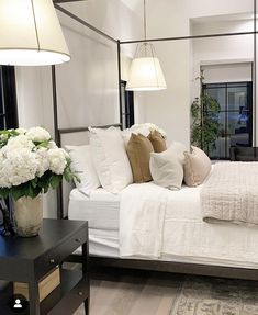 a white bed sitting in a bedroom next to a table with flowers on top of it