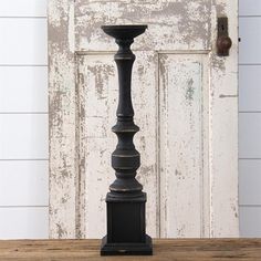 an old fashioned black candle holder on a wooden table in front of a white door