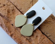 two tone drop earrings with black and white accents on a piece of wood next to a tag