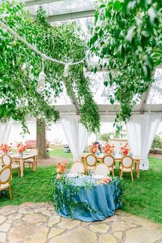 an outdoor venue with tables and chairs covered in blue cloths, greenery and flowers