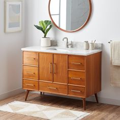 a bathroom vanity with a round mirror above it and a potted plant on the counter