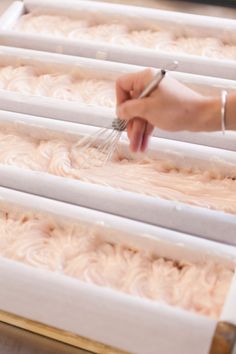 a person with a whisk in their hand on top of some white frosted cake