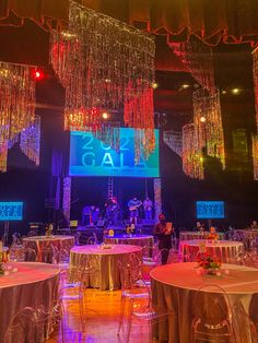 an indoor event with chandeliers, tables and chairs in front of a large screen