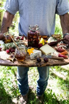 a man holding a tray with food on it in his hands and some cheeses