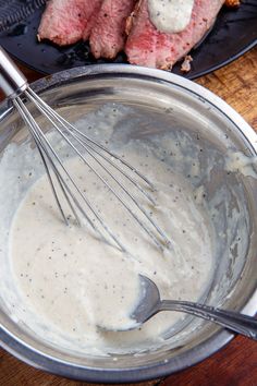 meat being whisked into sauce in a bowl on a wooden table with other food items