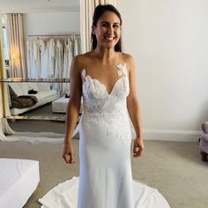 a woman in a white wedding dress standing next to a bed and looking at the camera