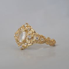 a gold ring with an oval shaped stone surrounded by small white stones and filigrees