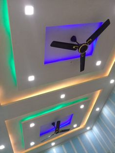 two ceiling fans mounted to the ceiling in a room with blue and green lights on it