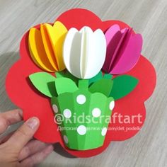 a hand holding up a paper flower on top of a wooden table with white dots