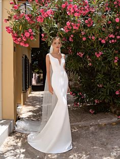 a woman in a white wedding dress standing next to some pink flowers and greenery