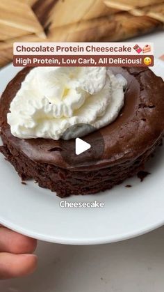 chocolate protein cheesecake with whipped cream on top, served on a white plate in front of bread basket