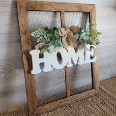 a wooden sign that says home with some greenery in it and the word home spelled out