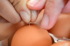 an egg being held by two hands over the top of another eggs shell with one hand