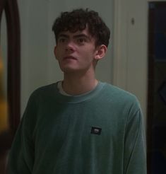 a young man standing in front of a mirror wearing a green shirt and looking at the camera