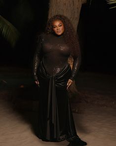 a woman standing in front of a tree wearing a black top and skirt with sequins on it