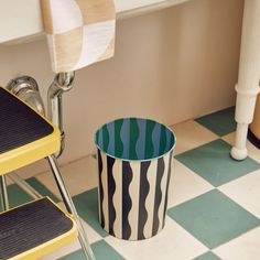 a black and white striped trash can sitting on the floor next to a yellow chair