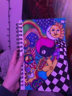 a person holding up a notebook with an artistic painting on it