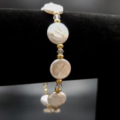 An elegant freshwater coin pearl clasp bracelet is ready to wear to a dressier event or be the perfect gift for someone lovely in your life. The bracelet includes flat, round 12 mm white pearl beads, clear bicone high-quality sparkly clear crystals, and delicate matte gold-colored glass spacer beads. The bracelet's clasp is a 14K gold-filled lobster clasp. The bracelet's stringing material is a high-quality, flexible gold-colored stringing wire. For added security, wire guards are placed on each Elegant Pearl White Stretch Bracelet, Adjustable Hypoallergenic Pearl Bracelet For Anniversary, Elegant White Crystal Bracelet For Anniversary, Round Pearl Crystal Bracelet For Gift, White Adjustable Beaded Bracelets For Formal Occasions, Classic White Jewelry With Round Stone, Elegant Hypoallergenic Name Bracelet With Round Beads, Elegant White Crystal Bracelet For Formal Occasions, White Jubilee Bracelet For Formal Occasions